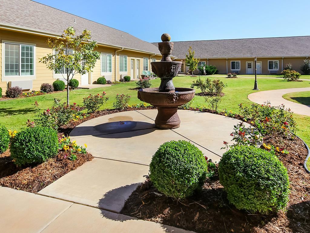 A beautifully landscaped courtyard featuring a central fountain surrounded by manicured shrubs and pathways.