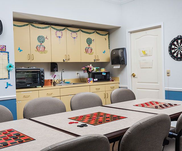 A break room with tables set up for checkers, surrounded by cabinets and kitchen appliances.