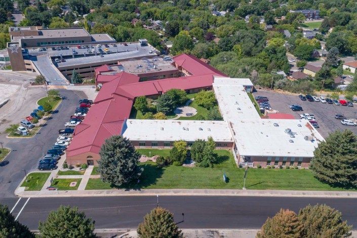Aerial view of a building with a red and white roof, surrounded by trees and a parking lot.