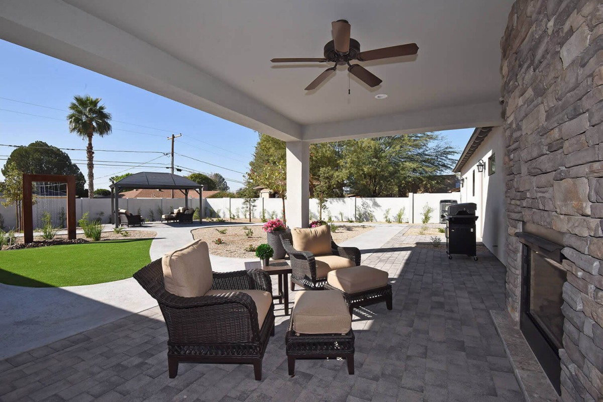 A cozy backyard patio with comfortable wicker furniture and a ceiling fan, perfect for outdoor relaxation.