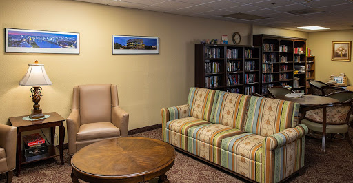 A cozy living room space featuring a striped sofa, an armchair, a wooden coffee table, and a bookshelf filled with books.