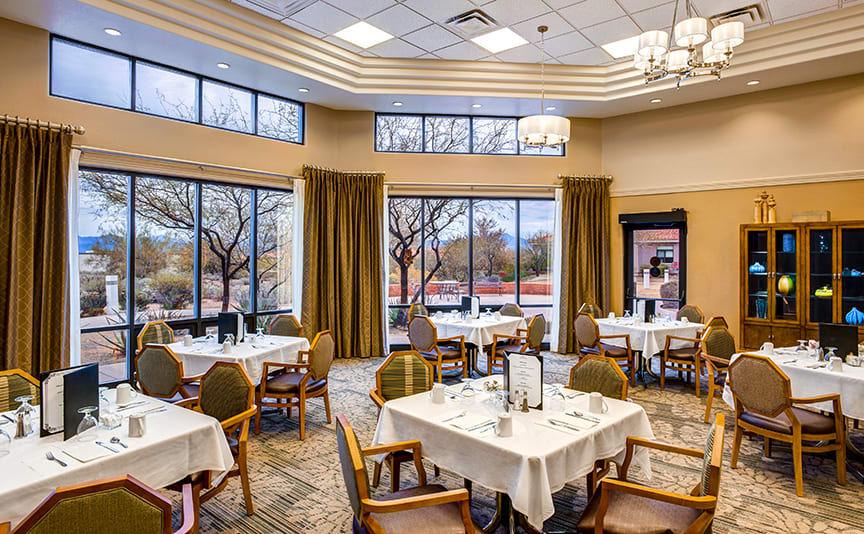 A well-appointed dining area with neatly arranged tables and chairs, large windows, and elegant lighting.