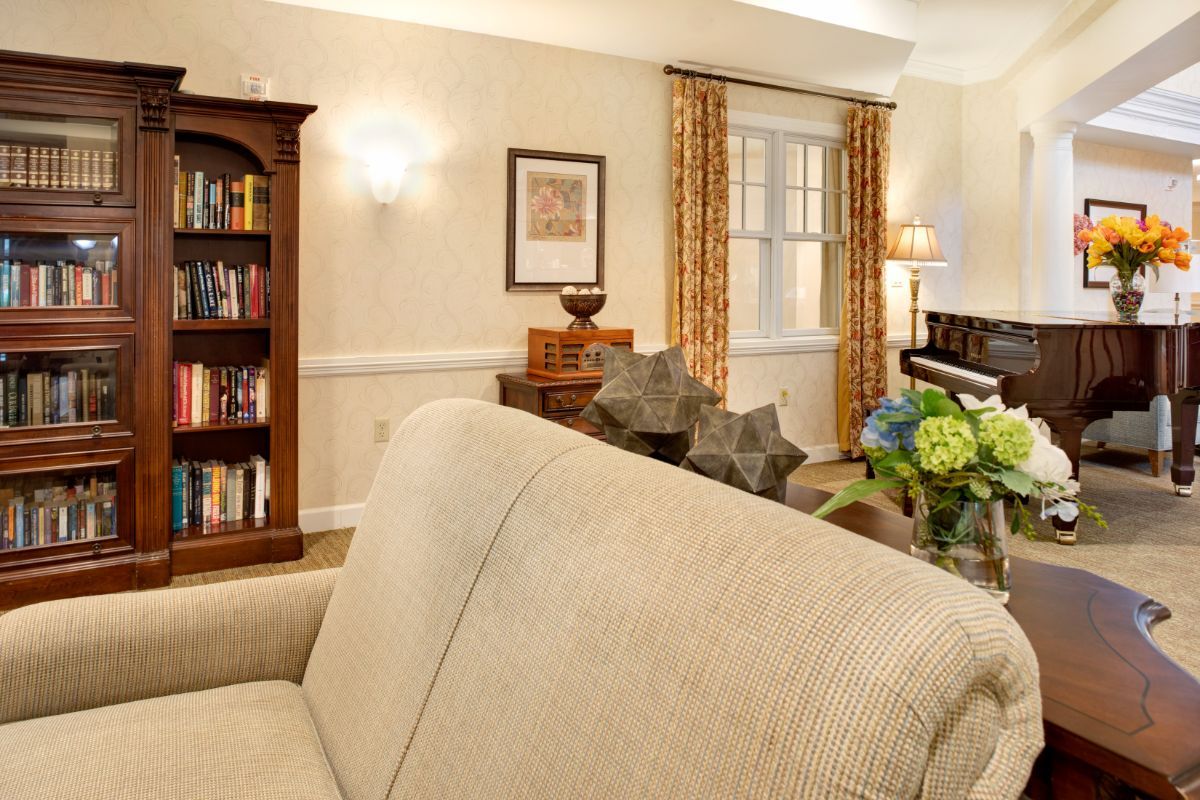 A cozy living room with elegant decor, featuring a sofa, bookshelf, piano, and warm lighting.