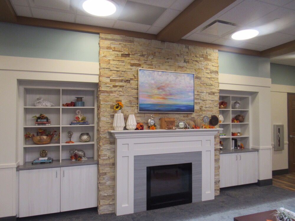 A cozy living room featuring a stone fireplace with decorative shelves and artwork above.