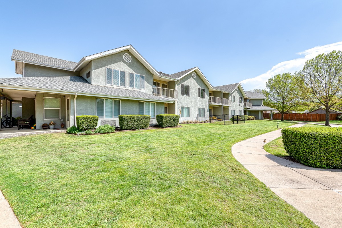 A modern apartment complex with well-maintained green lawns and a walkway on a sunny day.