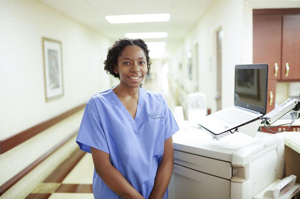 A nurse standing in a hospital corridor wearing blue scrubs.