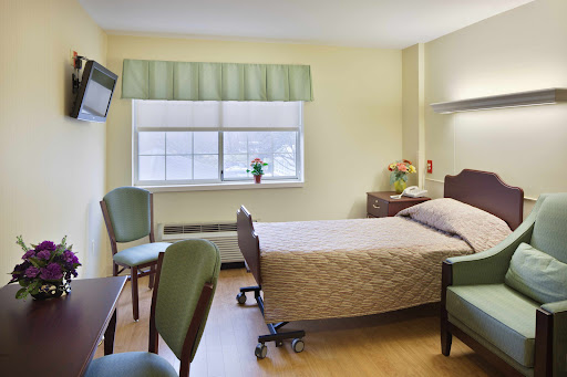 A tranquil hospital room featuring a bed, seating area, and natural light.