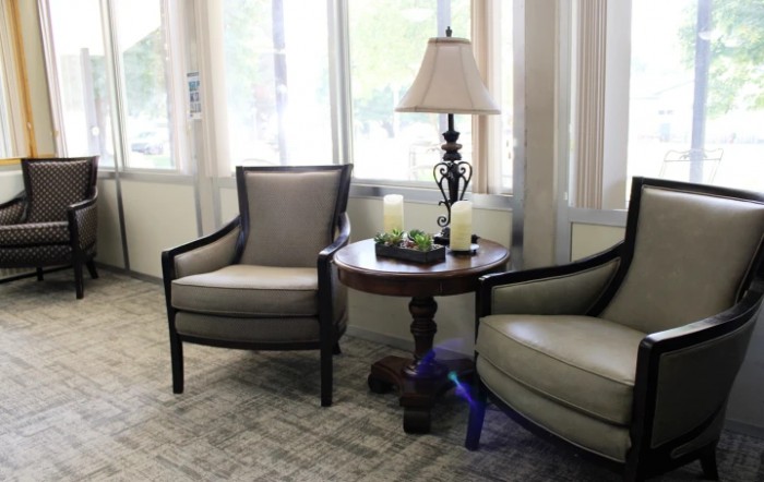 A cozy seating area featuring two armchairs, a round wooden table, and a decorative lamp by the window.