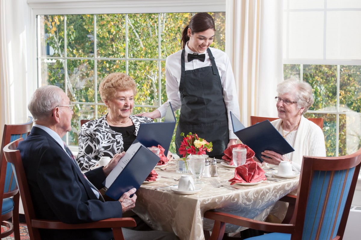 A group of seniors seated at a restaurant table with a waitress taking their order.