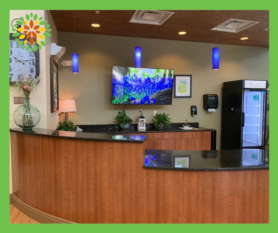 A welcoming reception area with a wooden desk, plants, and a television mounted on the wall.