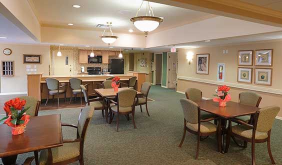 A community dining area with several tables and chairs, adjacent to a kitchen.
