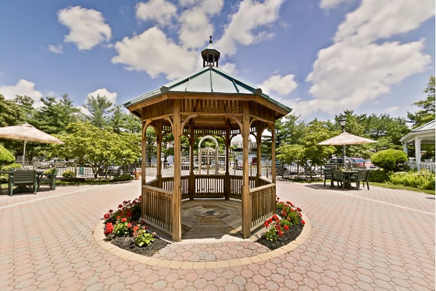 A wooden gazebo surrounded by flowers in a park setting on a sunny day.