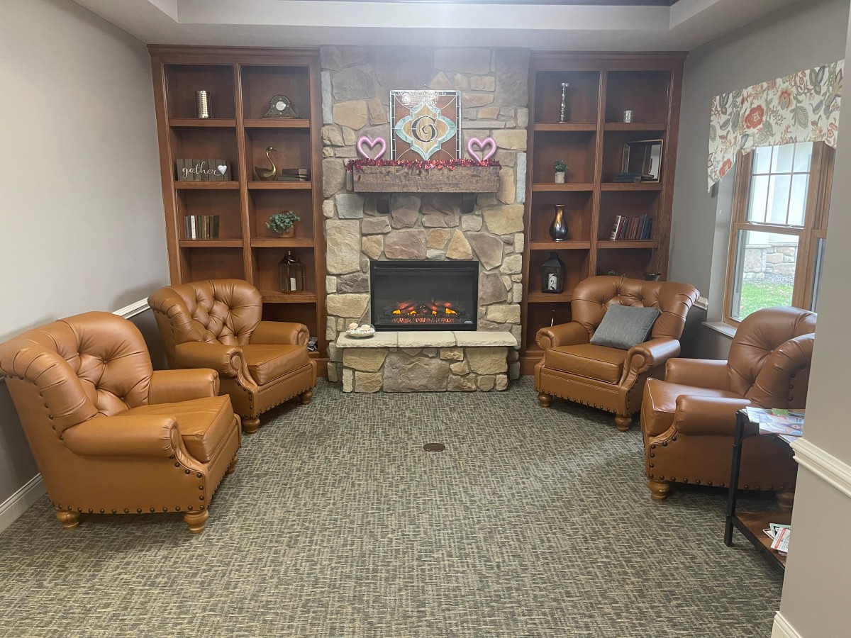 A cozy living room with a central fireplace surrounded by leather armchairs and wooden bookshelves.