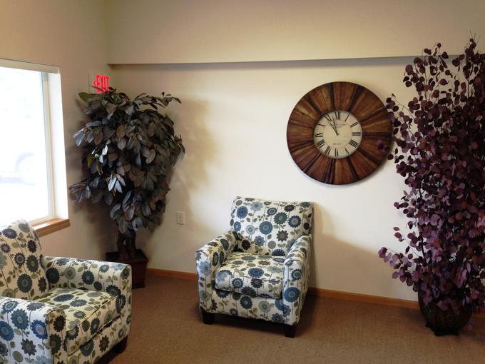 A cozy seating area featuring two patterned chairs, large decorative clock, and potted plants.