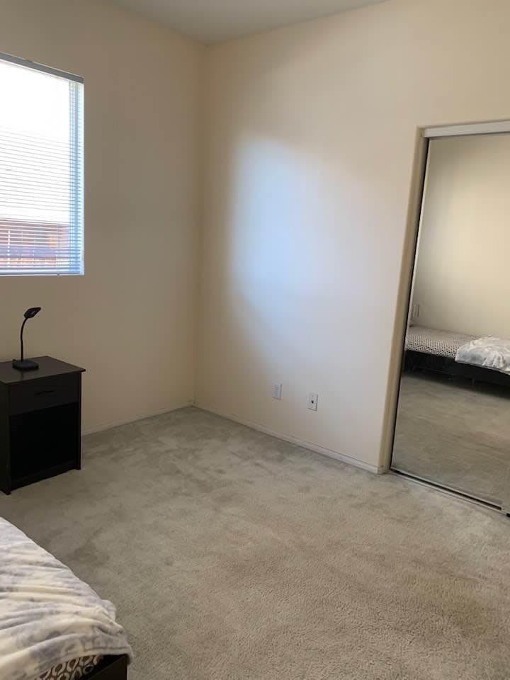 A minimalist bedroom with a bed, nightstand, lamp, and mirrored closet.