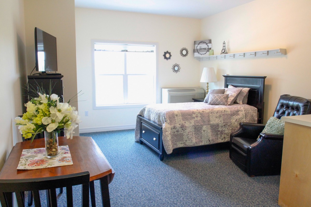 A cozy bedroom with a neatly made bed, a window letting in natural light, and simple decor.