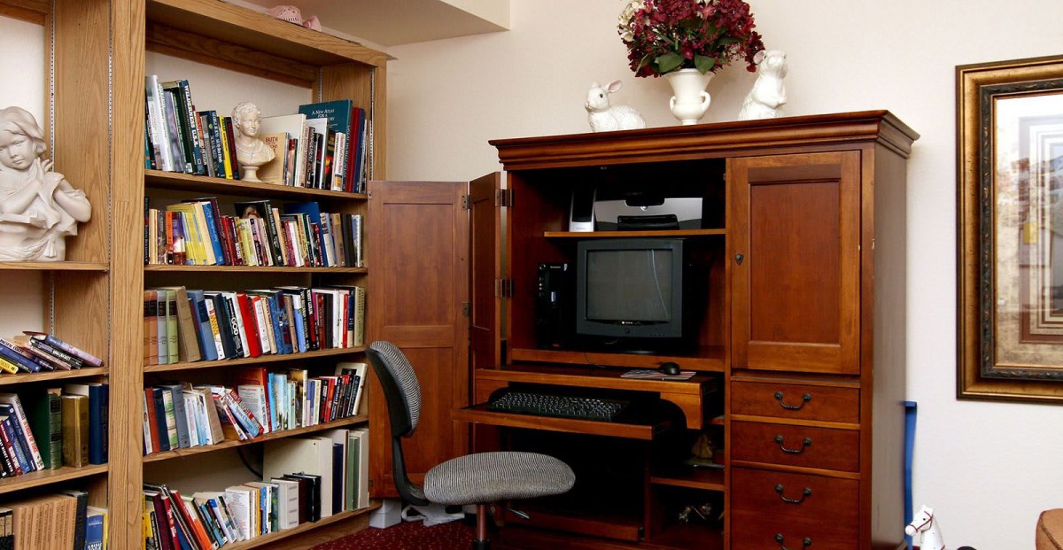 A cozy home office setup with a wooden desk, chair, and bookshelf filled with books.