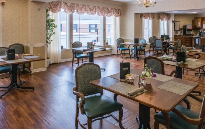A cozy dining area with neatly arranged tables and chairs, featuring large windows and elegant decor.