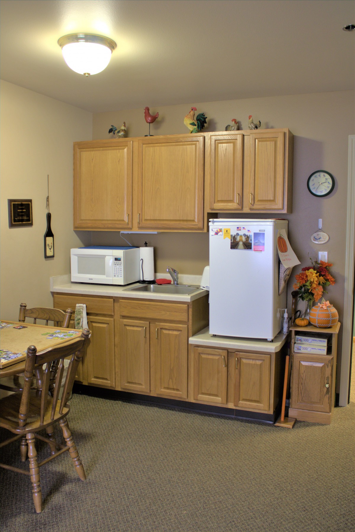 A small kitchen with wooden cabinets, a fridge, and a microwave placed on the countertop next to a dining table.