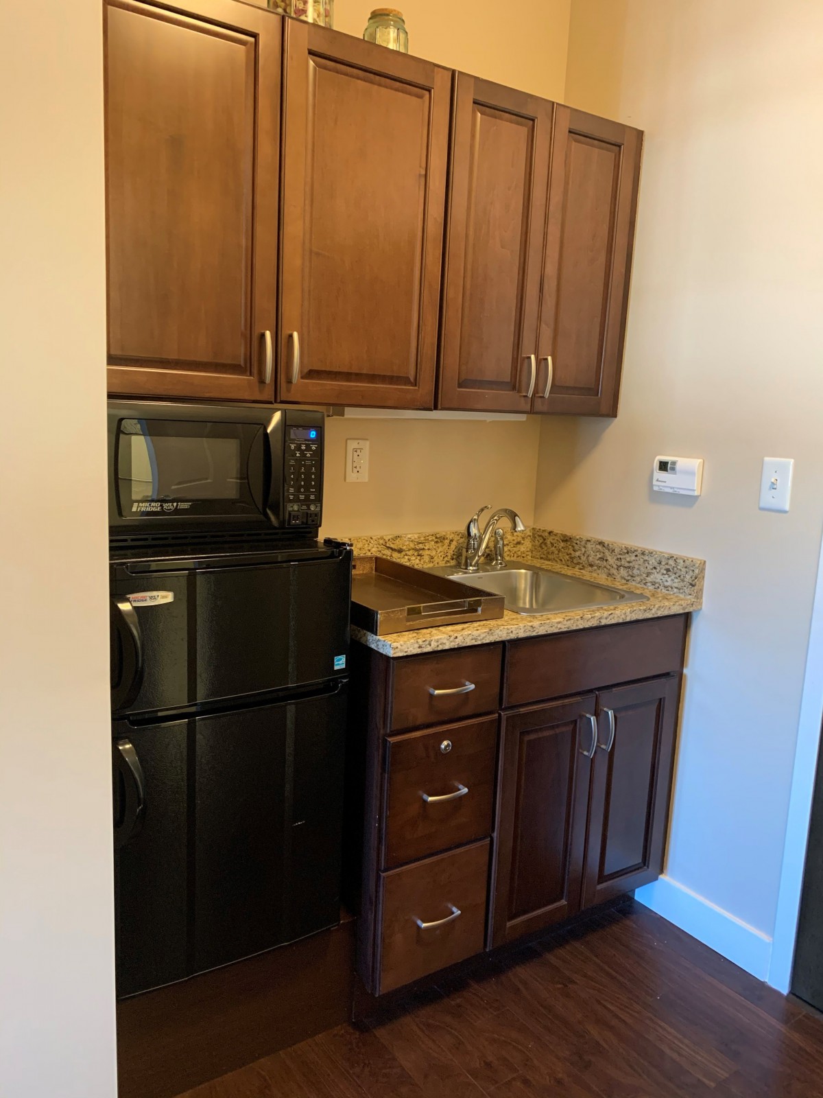 A compact kitchen area featuring a microwave, refrigerator, and wooden cabinets.