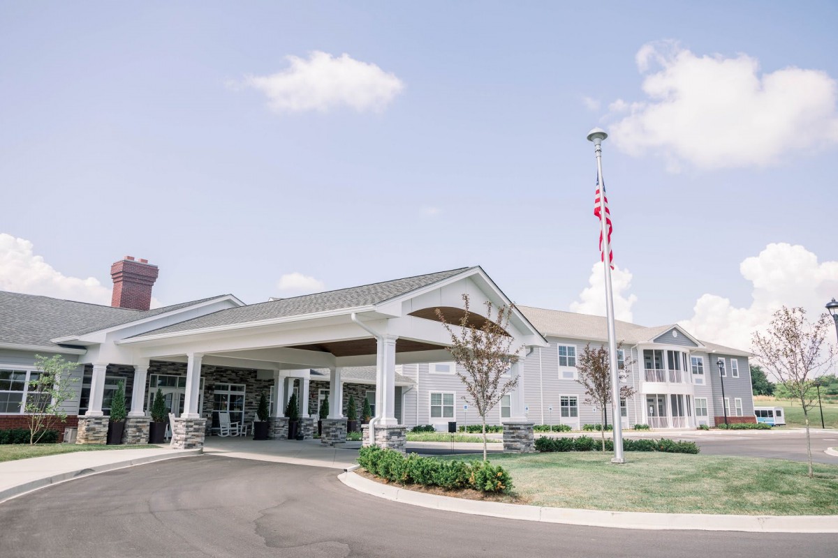 A sunny day view of a building entrance with a flagpole and well-maintained landscaping.