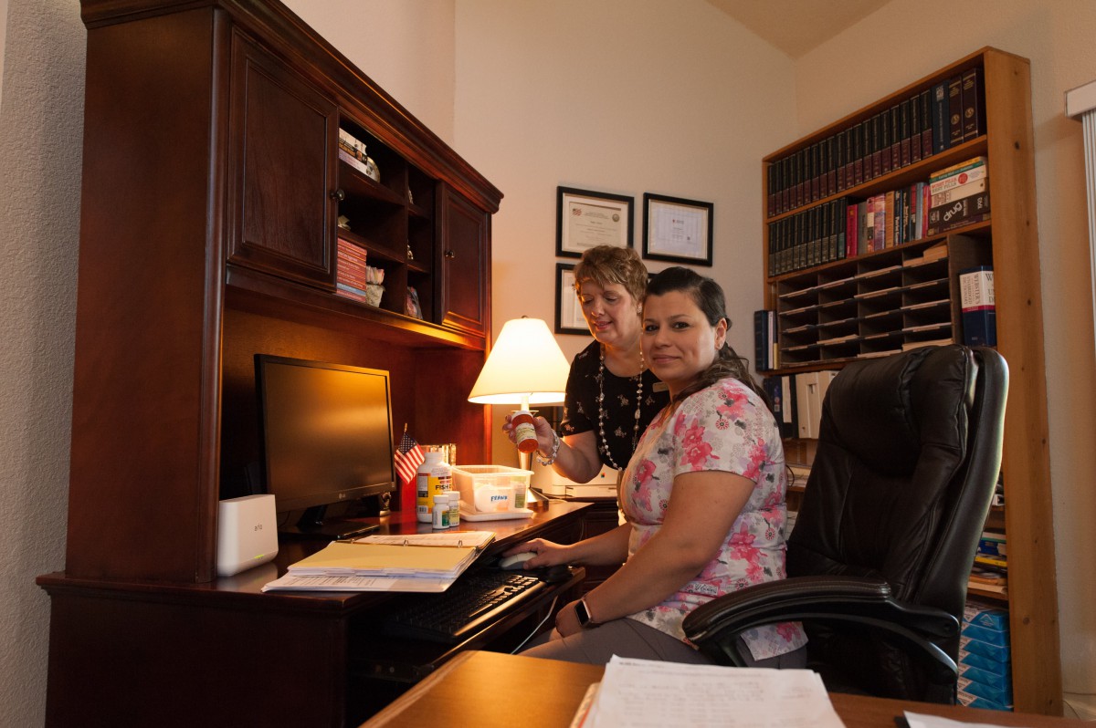 Two people working at a desk in an office setting with books and a computer.
