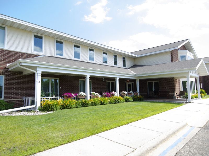 A residential building with a well-maintained lawn and colorful flowers under a partly cloudy sky.