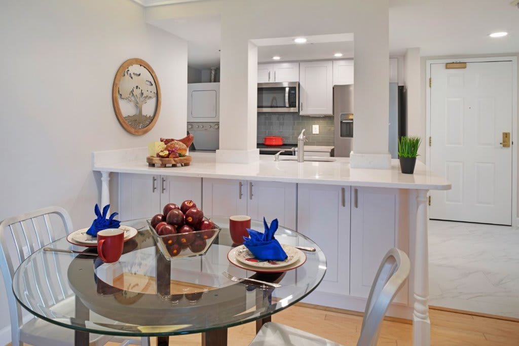 A modern kitchen and dining area with white cabinets and a glass table set for a meal.