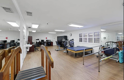 A spacious physical therapy room equipped with exercise machines, rehabilitation bars, and a workspace.