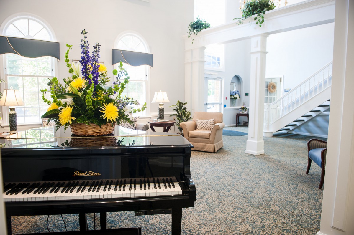 A spacious and inviting living room featuring a grand piano, floral arrangement, and cozy seating.