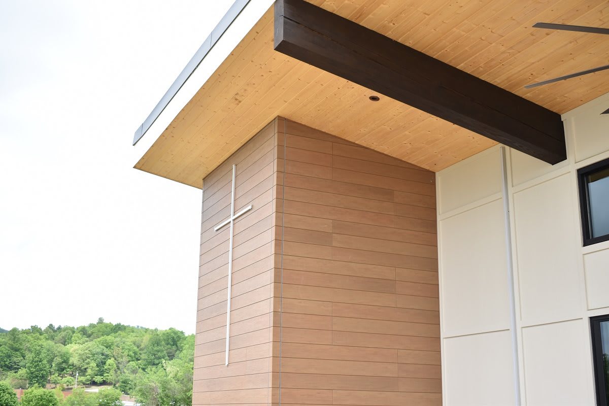 A modern church exterior with wood paneling and a cross.
