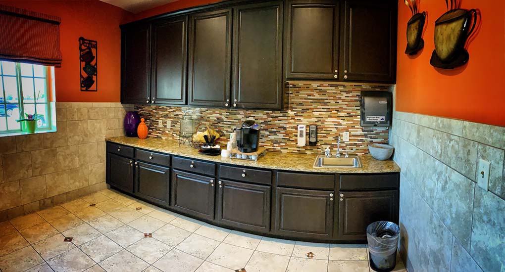 A modern kitchen with dark cabinets, a stone backsplash, and various appliances on the countertop.