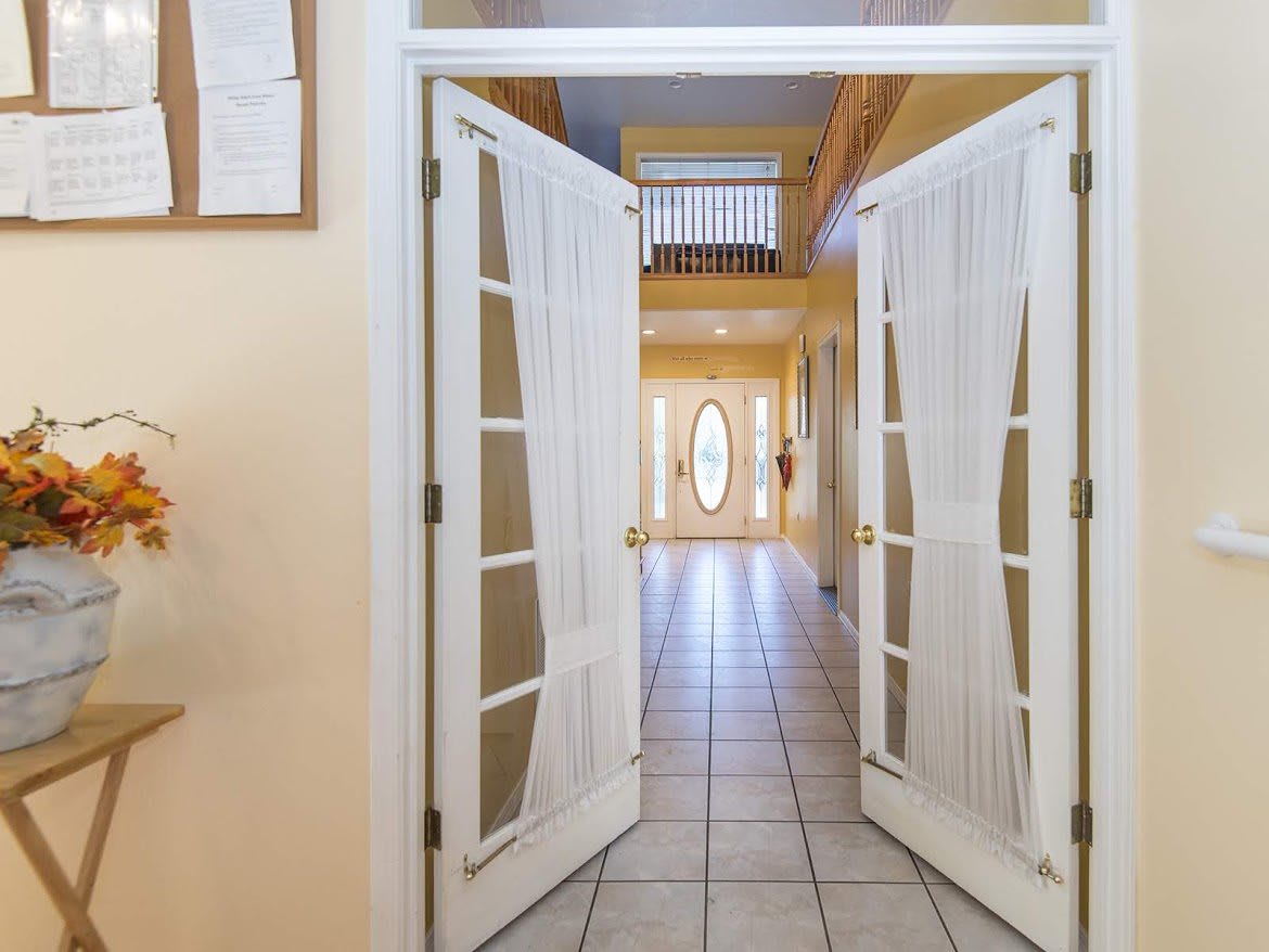 A view of a bright residential hallway with double doors and tiled flooring.