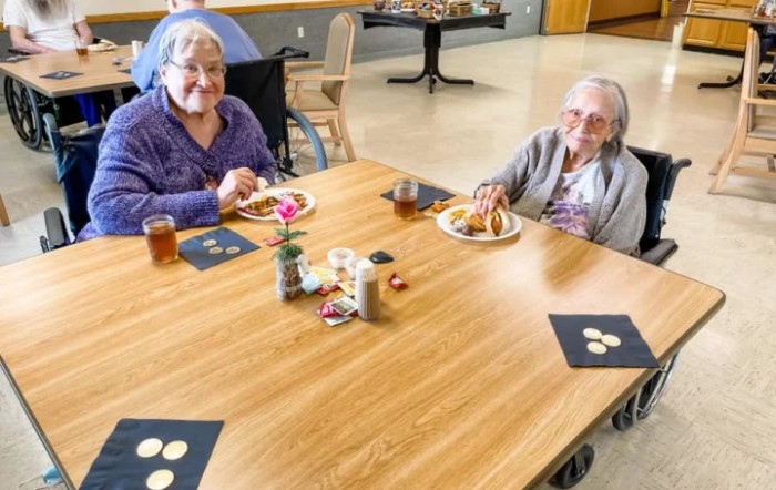 Two elderly women enjoying a meal together at a dining table indoors.