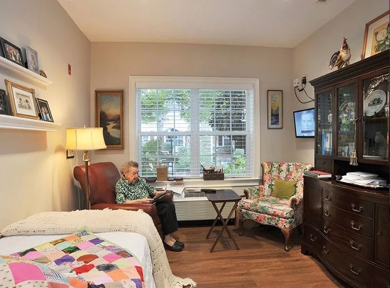 An elderly person reading in a cozy living room with comfortable furniture and a large window.