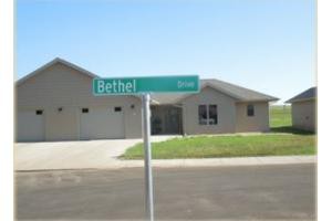 A suburban street with a green street sign labeled 'Bethel' in front of a single-story house.
