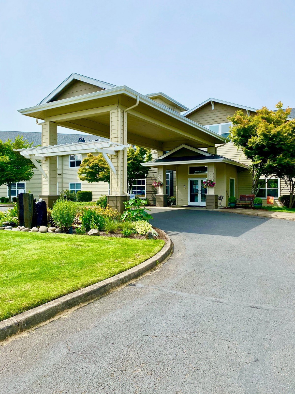 A well-maintained building entrance with landscaped surroundings and a driveway.
