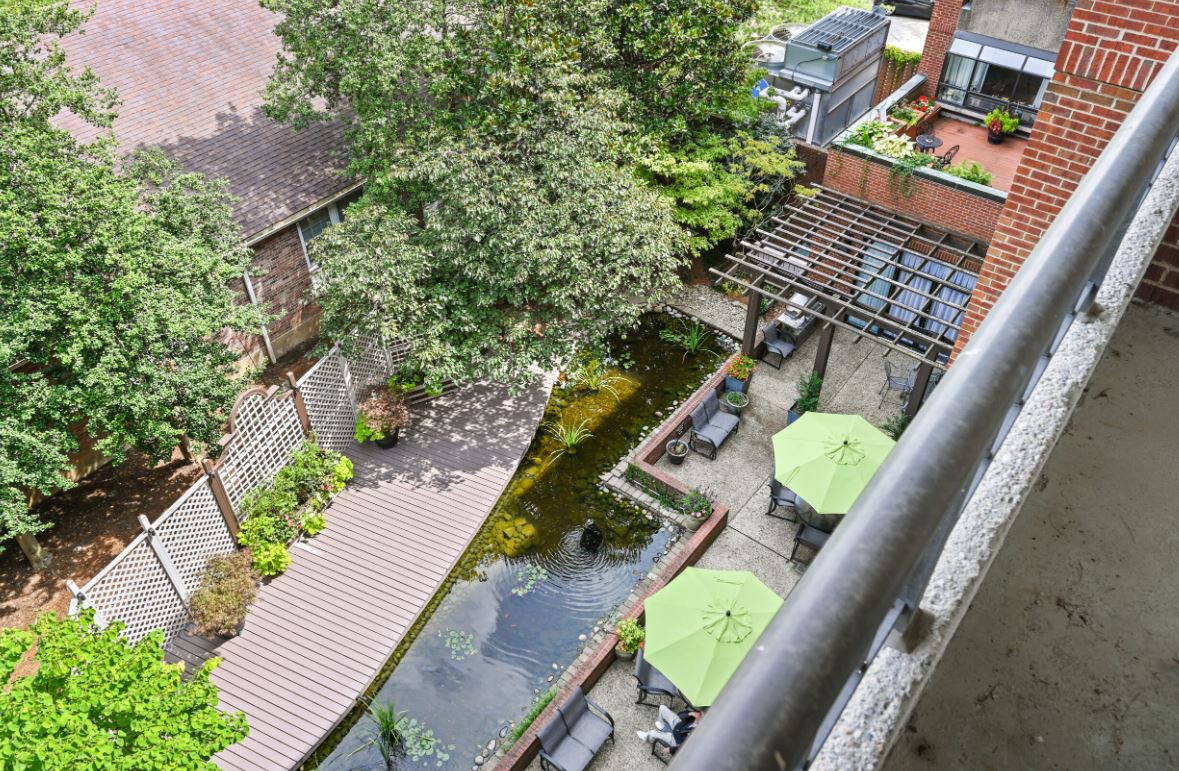 A serene garden view with a pond and outdoor seating area featuring green umbrellas.