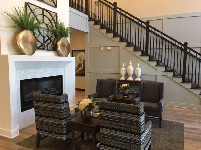 A modern living room featuring a cozy seating area with striped chairs and a sofa, accented by decorative vases and a staircase in the background.