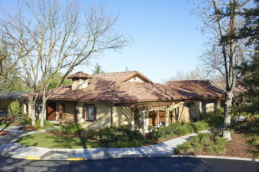 A suburban residential house with a tile roof and surrounding trees on a sunny day.