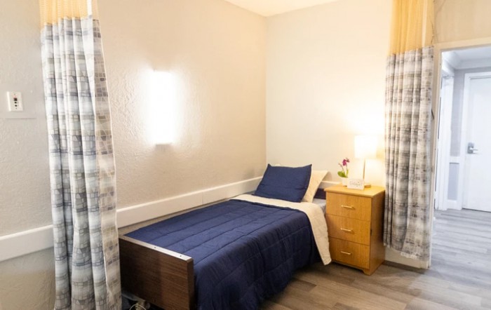 A simple and cozy bedroom with a single bed, nightstand, and soft lighting.