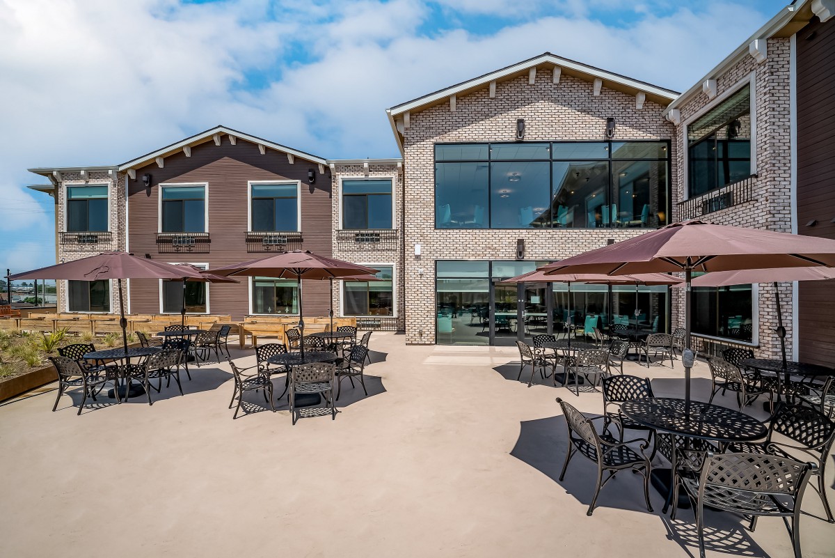 An outdoor patio area with tables and chairs, shaded by umbrellas, outside a modern building.