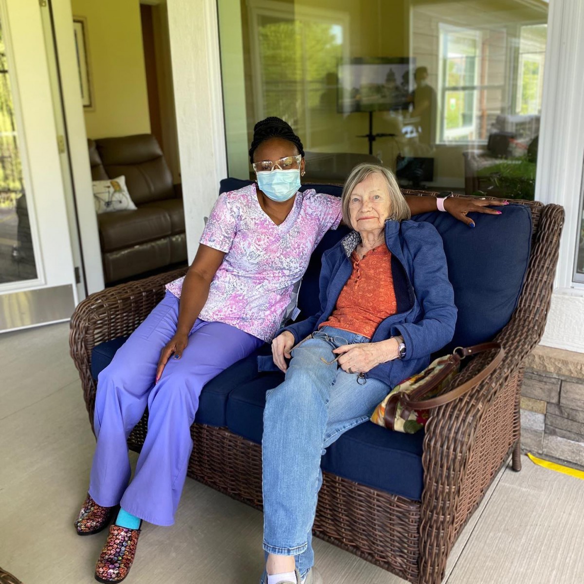 A healthcare worker and an elderly person sitting together on an outdoor patio.