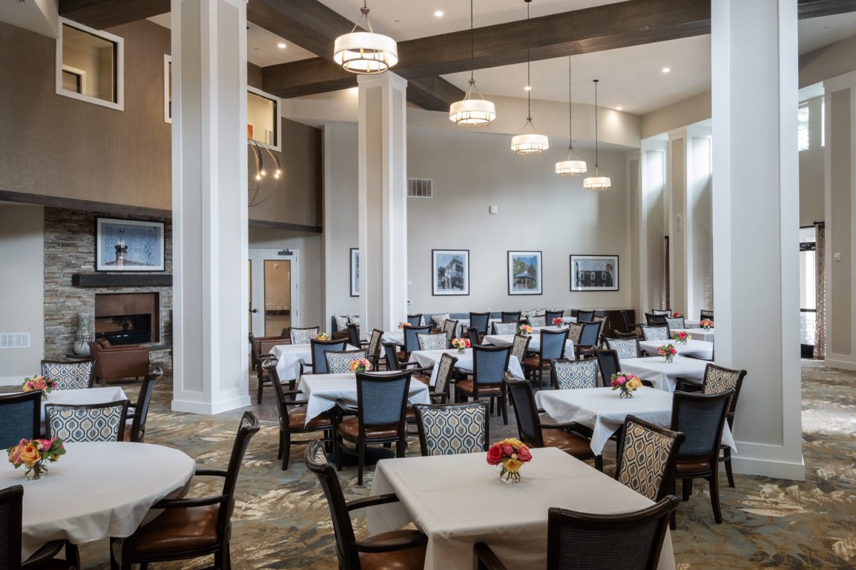 A spacious dining room with neatly arranged tables and chairs, elegantly lit by overhead lights.