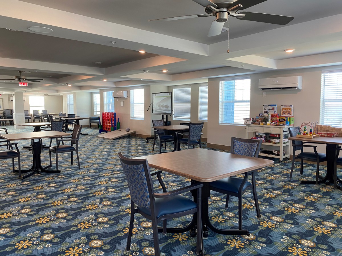 A spacious dining area with several tables and chairs, featuring decorative carpet and ample lighting.