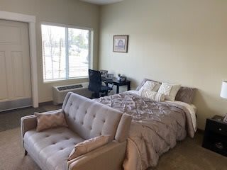 A cozy bedroom with a bed, sofa, and desk by the window.