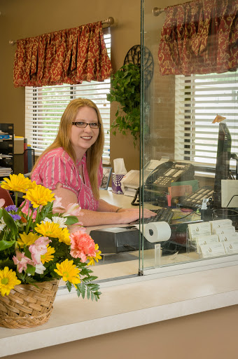 A friendly receptionist at her desk surrounded by vibrant flowers.