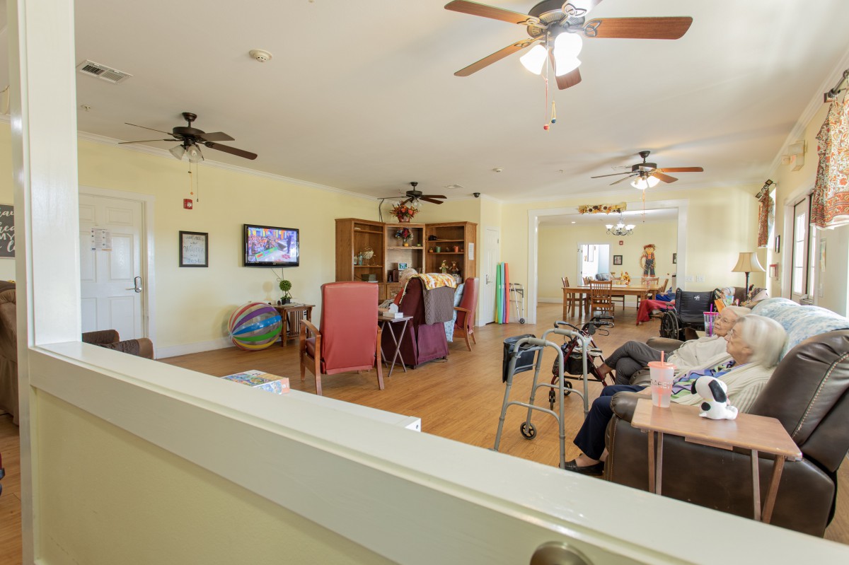 A spacious living room with furniture, ceiling fans, and people engaging in activities.