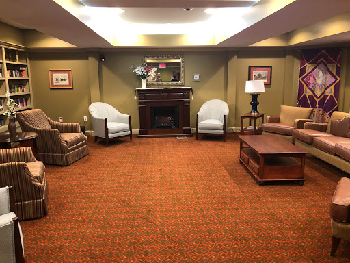 A cozy lounge area featuring comfortable seating, a fireplace, and warm carpeting.