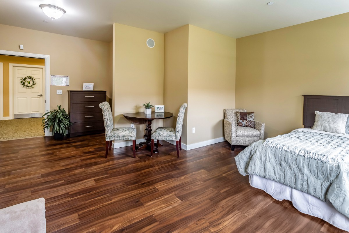 A well-furnished bedroom with hardwood flooring, featuring a bed, a small round table with chairs, and an armchair.